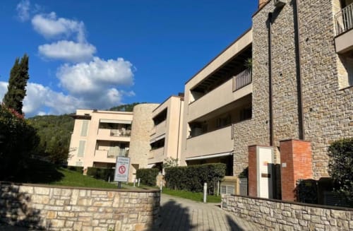 Modern apartment complex in Como, Tuscany with stone facades, balconies, and lush grounds under blue sky