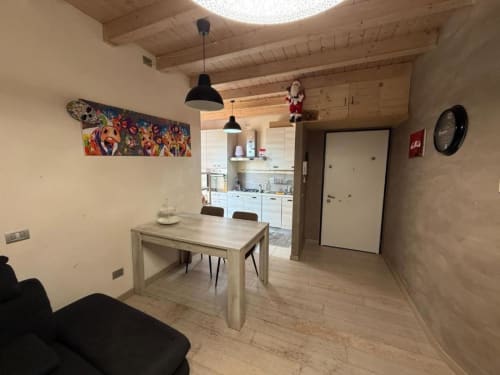 Modern apartment dining area in Versilia Panoramic Luxury, Toscana, with wooden beams, light wood table, and open kitchen.