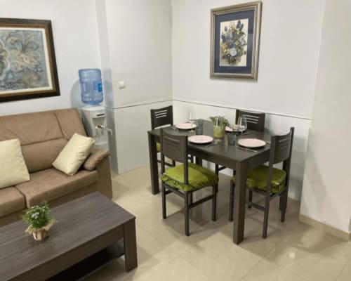Modern apartment living and dining area with beige sofa, black dining table, green cushions, and framed botanical art in