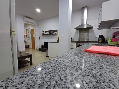 Modern kitchen with granite countertop, stainless steel range hood, and open-plan living area in Algemesi Home apartment