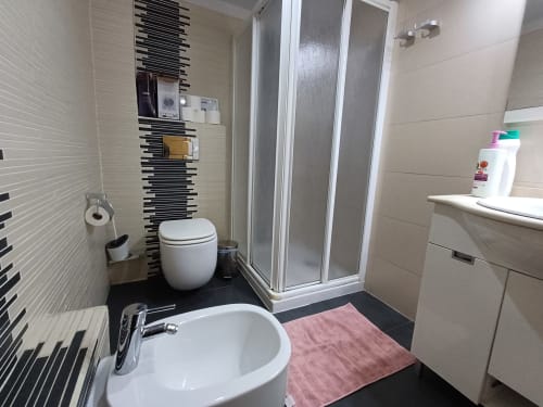 Modern bathroom at Algemesi Home apartment with white sink, toilet, shower enclosure, and black and white tile accents