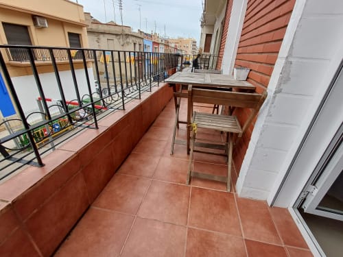 Terrace with red tile flooring, wooden furniture, and black railing overlooking Algemesí city buildings