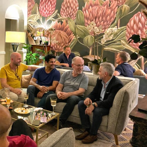 Hommes en train de socialiser dans le salon de l'hôtel Cinq & Sept avec œuvres florales, boissons et zone de détente