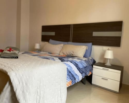 Modern bedroom at Algemesi Home apartment with dark wood headboard, blue bedding, white nightstand, and lamp