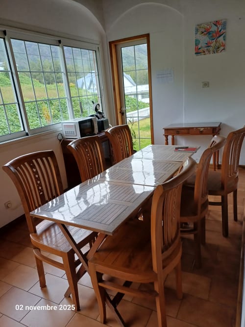 Salle à manger lumineuse à la Porte de Mafate avec mobilier en bois, vue montagne par les grandes fenêtres et carrelage en terre cuite