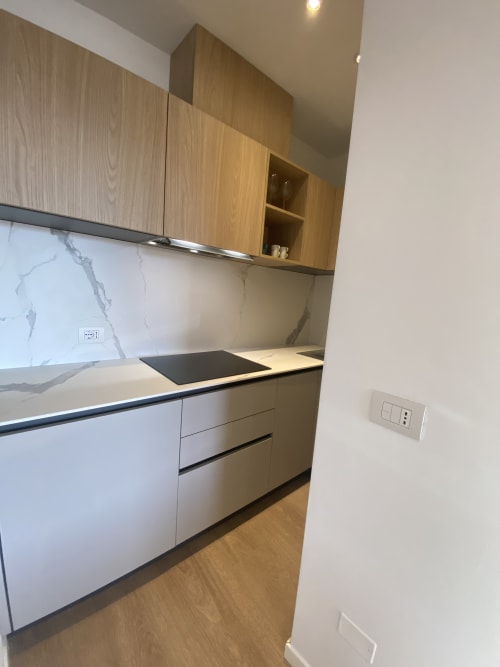 Modern kitchen with wood cabinetry, marble backsplash, and built-in appliances in Rimini apartment