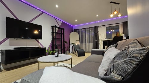 Suite Diamond moderne à la Résidence L'Hermitière avec plafond LED violet, téléviseur écran plat, canapé gris, table ronde blanche et