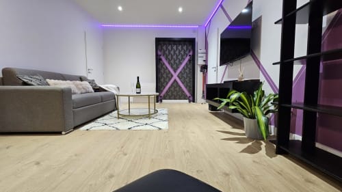 Suite loveroom Diamond moderne à la Résidence L'Hermitière : canapé gris, ambiance néon violet, parquet, TV et spa