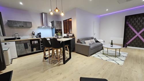 Appartement moderne ouvert à la Résidence L'Hermitière avec cuisine équipée, coin repas, canapé gris et accent violet