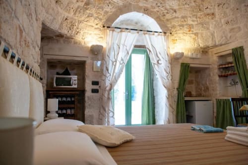 Camera Trulli Boccadoro con soffitto in pietra arcuato, letto in legno, tende verdi e porta ad arco in B&B italiano