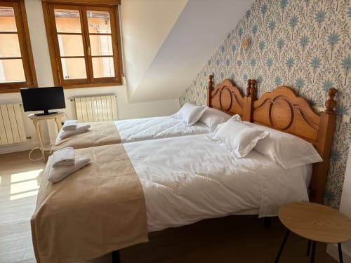 Acogedora habitación en Pensión Argüelles de Ribadesella con cama de madera, ropa blanca y papel pintado estampado