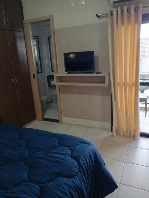 Quarto moderno do hotel Wellington Rodovalho em Goiânia com cama azul, TV, banheiro e vista da cidade