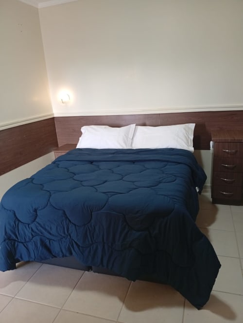 Quarto moderno do hotel Wellington Rodovalho em Goiânia com cama queen, edredom azul-marinho, almofadas brancas e madeira escura