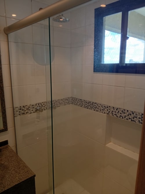Chuveiro moderno envidraçado com azulejos brancos tipo metrô e fita decorativa de pedrinhas no apartamento Wellington Rodovalho em