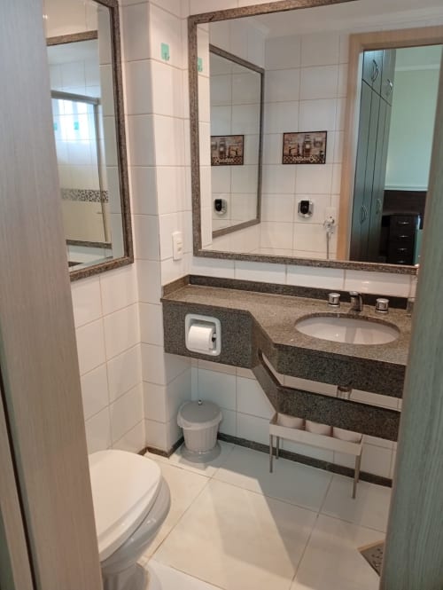 Banheiro moderno no apartamento Crystal Place do hotel Wellington Rodovalho, Goiânia, com bancada em granito e espelhos