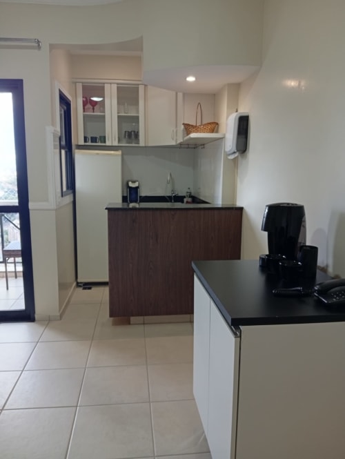 Cozinha moderna do hotel Wellington Rodovalho em Goiânia, com armários em madeira escura, móveis altos brancos e bancada preta