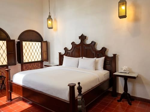 Elegant bedroom at Villa Merida Boutique Hotel in Merida with ornate wooden bed, white linens, terracotta tile floor, and