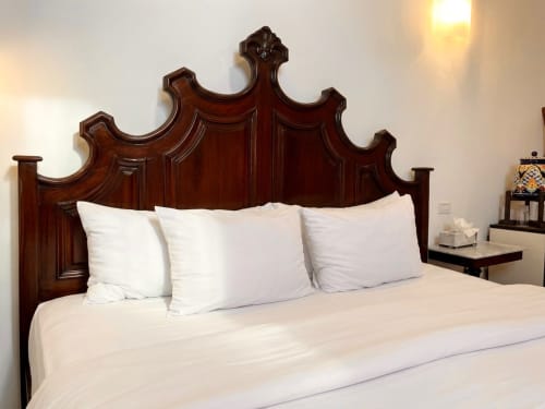 Elegant bedroom at Villa Merida Boutique Hotel in Merida with ornate wood headboard and white linens
