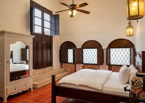 Luxurious bedroom at Villa Merida Boutique Hotel in Merida with colonial wood furnishings, arched windows, and pool view