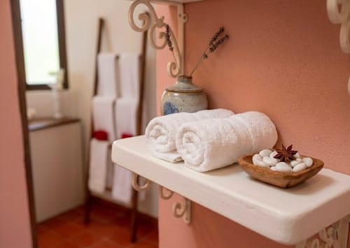 Spa bathroom shelf at Villa Merida Boutique Hotel with rolled white towels, lavender decor, and wooden bowl in Merida