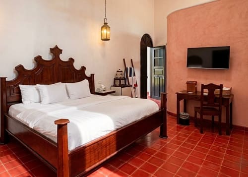 Elegant bedroom at Villa Merida Boutique Hotel with carved wooden bed, terracotta tiles, and colonial-style decor in Merida
