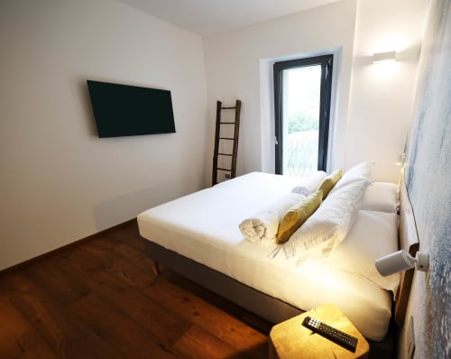 Modern bedroom at La Casa nel Bosco with white bed, flat-screen TV, wooden floors, and garden view balcony in Somma Lombardo
