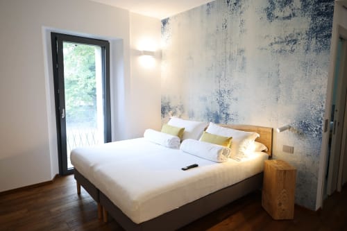 Modern bedroom at La Casa nel Bosco in Somma Lombardo with wood bed, white linens, textured accent wall, and garden view