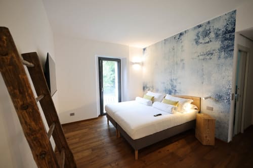 Modern bedroom at La Casa nel Bosco with queen bed, wooden nightstands, rustic ladder, textured accent wall, and garden view