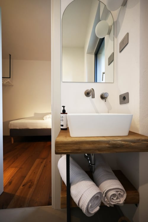Modern bathroom with white vessel sink on wooden vanity, arched mirror, and rolled towels at La Casa nel Bosco B&B