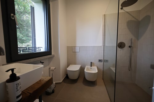 Modern bathroom at La Casa nel Bosco B&B in Somma Lombardo with walk-in shower, bidet, toilet, and window overlooking garden