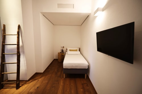 Compact bedroom at La Casa nel Bosco with single bed, flat-screen TV, wooden ladder shelf, and hardwood flooring in Somma