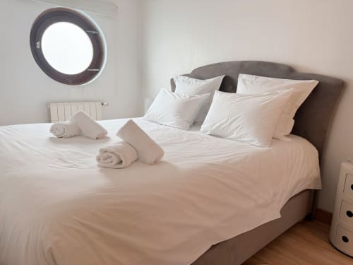 Chambre luxueuse de la Villa Eleonore à la Maison ARLOÉ, La Rochelle avec draps blancs, serviettes roulées et tête de lit grise.