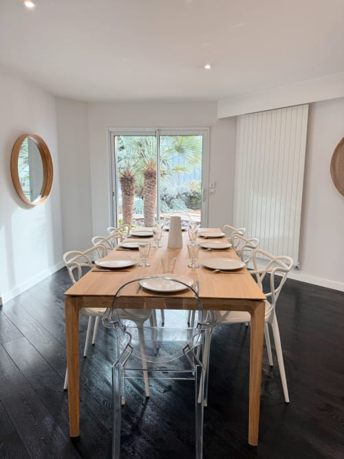 Salle à manger moderne de la Villa Eleonore avec table en bois, chaises blanches et vue sur le jardin planté de palmiers à La Rochelle