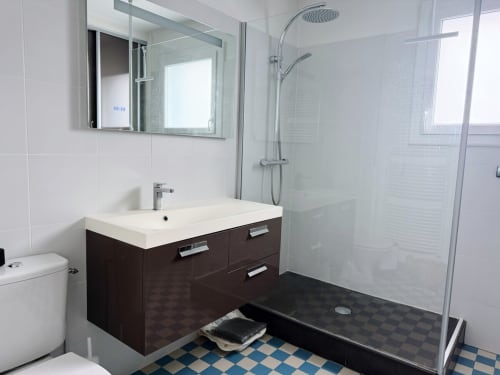 Salle de bain moderne avec vanité noire, lavabo blanc, miroir illuminé, douche en verre et carrelage bleu et blanc à damier