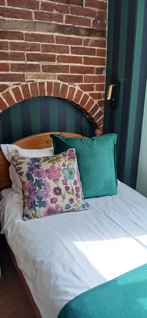St Mary's Street bedroom at Earsham Street House, Bungay, with floral and teal pillows on a wooden bed against exposed brick
