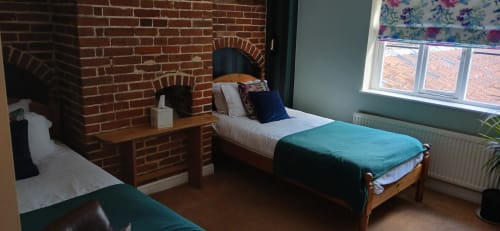 Cozy bedroom at Earsham Street House in Bungay with twin beds, exposed brick fireplace, and large window