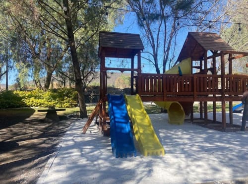Estructura de juegos infantiles de madera con toboganes azul y amarillo en Hotel El Porvenir, rodeada de árboles y jardines en Querétaro