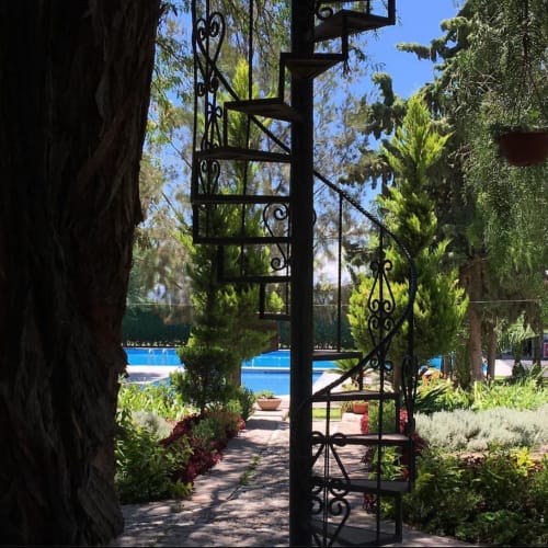 Ornamentada puerta de hierro enmarcando sendero jardín exuberante con vista a piscina en villa Hotel El Porvenir