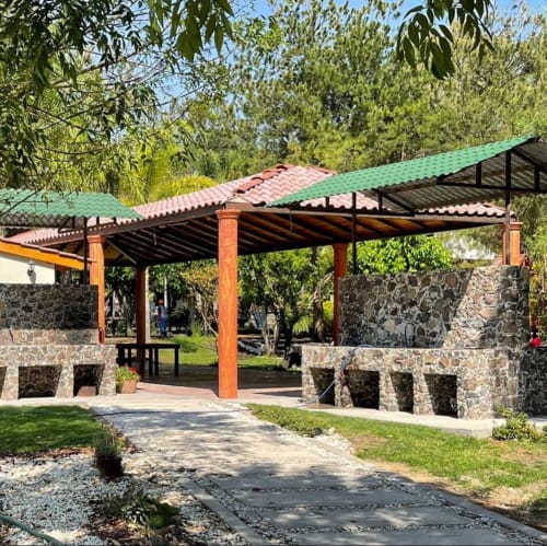 Rústico pabellón techado con muros de piedra y techo de tejas rojas en la villa jardín de Hotel El Porvenir en Querétaro, México