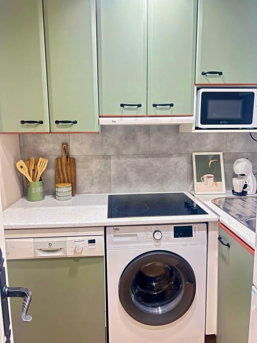 Cocina moderna con gabinetes blancos, azulejos grises, placa de inducción, lavadora y utensilios de madera en Era Clau Homes