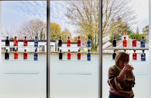 The Corries B&B window display in Alexandria showcasing colorful spirit bottles with Luss countryside views