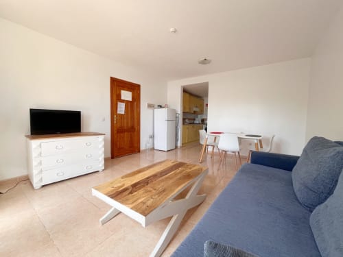 Moderna zona de estar abierta en FTV Holidays Homes en La Oliva con sofá gris, mesa de comedor y cocina