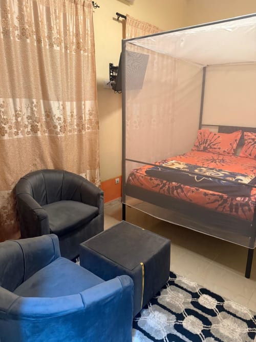 Chambre cosy de Keur Medzo avec fauteuil noir, literie orange et rideaux crème à Lac Rose, Niaga