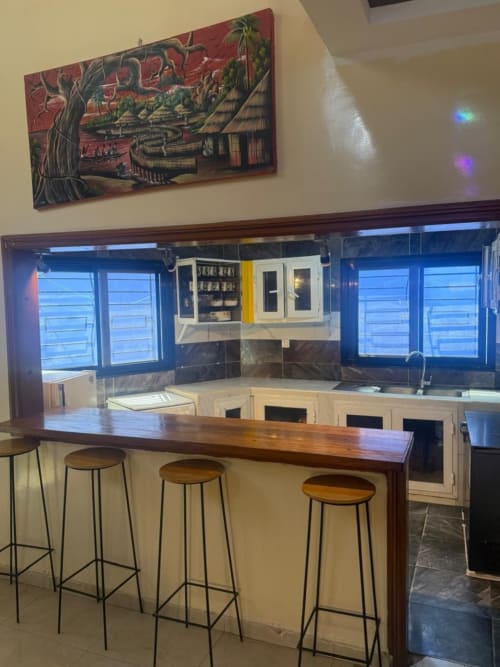Bar de l'hôtel avec comptoir en bois, tabourets de bar et cuisine avec miroir à Keur Medzo, Lac Rose