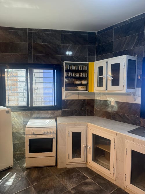 Cuisine moderne à Keur Medzo Lac Rose avec carrelage en marbre noir, placards en bois, cuisinière et rangements muraux à Niaga