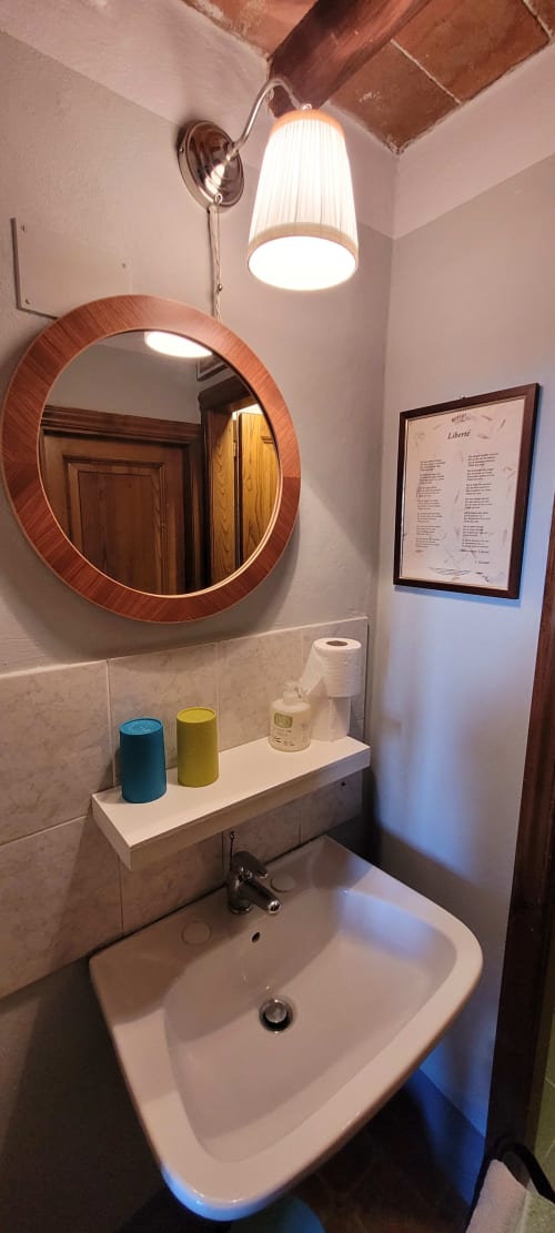 Modern bathroom in Mimosa e Olivo room at Rendola Riding, Montevarchi with circular wooden mirror and pendant lighting