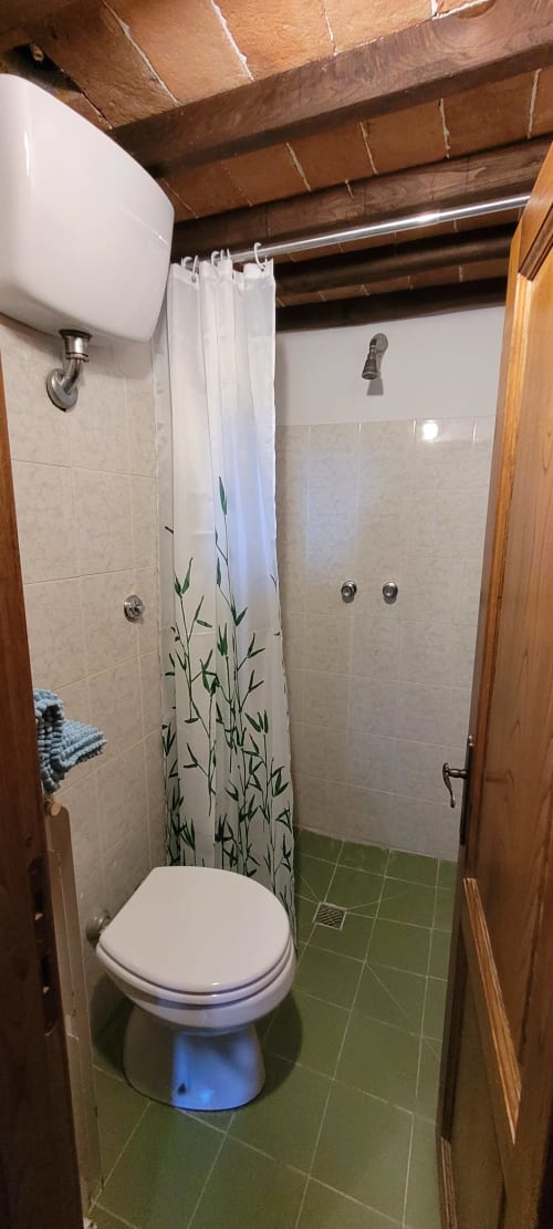 Shared bathroom in Mimosa e Olivo room at Azienda Agricola Rendola Riding, featuring toilet, shower, beige tiles, and exposed