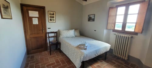 Cozy bedroom at Rendola Riding in Montevarchi with double bed, wooden door, window with landmark view, and rustic terracotta