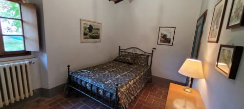 Mimosa e Olivo bedroom at Azienda Agricola Rendola Riding, Italy with wrought iron bed, desk lamp, and terracotta flooring