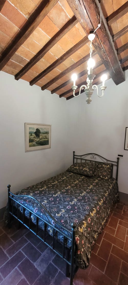 Rustic bedroom with exposed wooden beams, wrought iron bed, floral bedding, and chandelier at Rendola farm stay in Tuscany